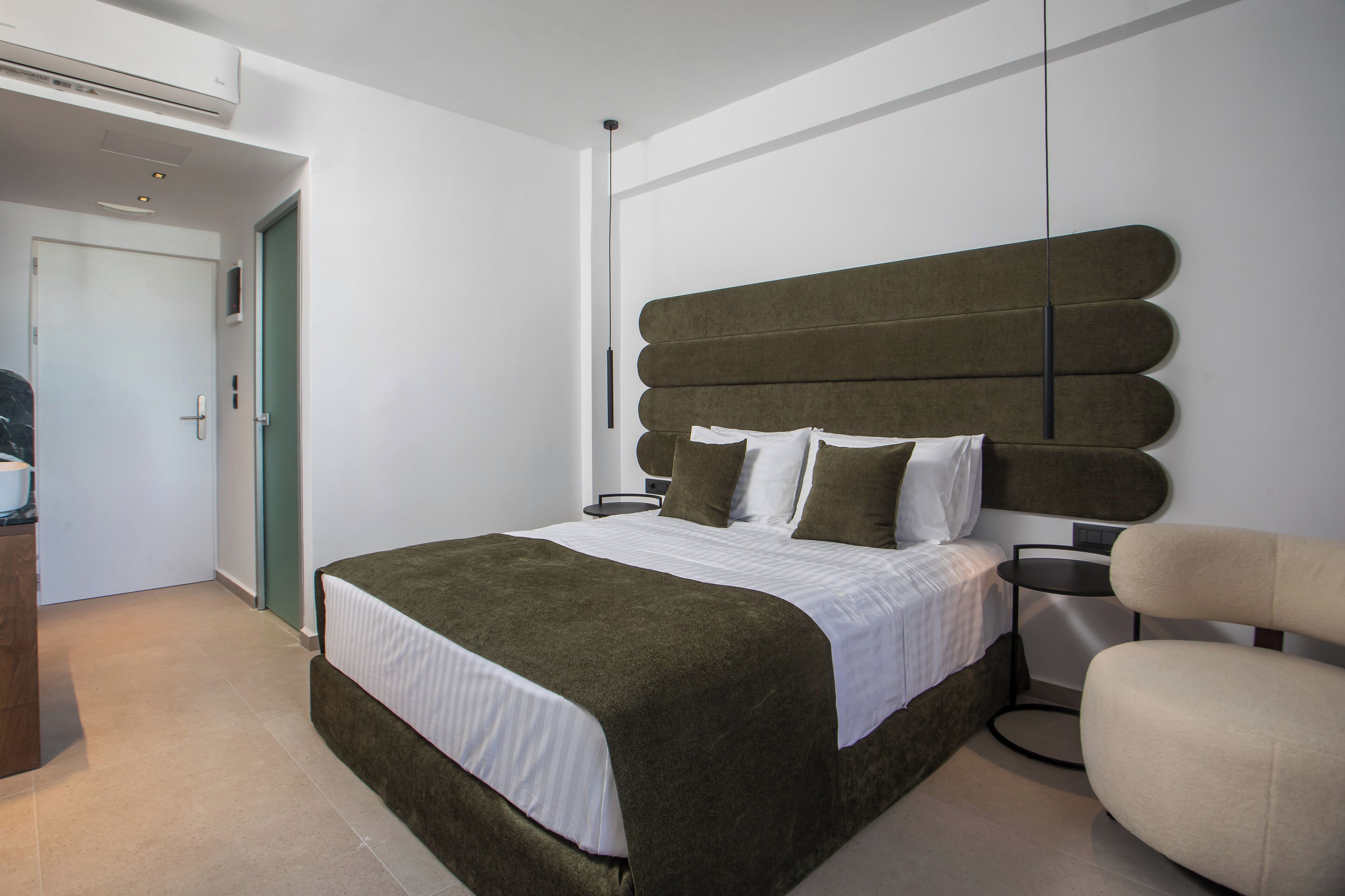 A modern bedroom with a large bed, a bedside table, a chair, and a door.
