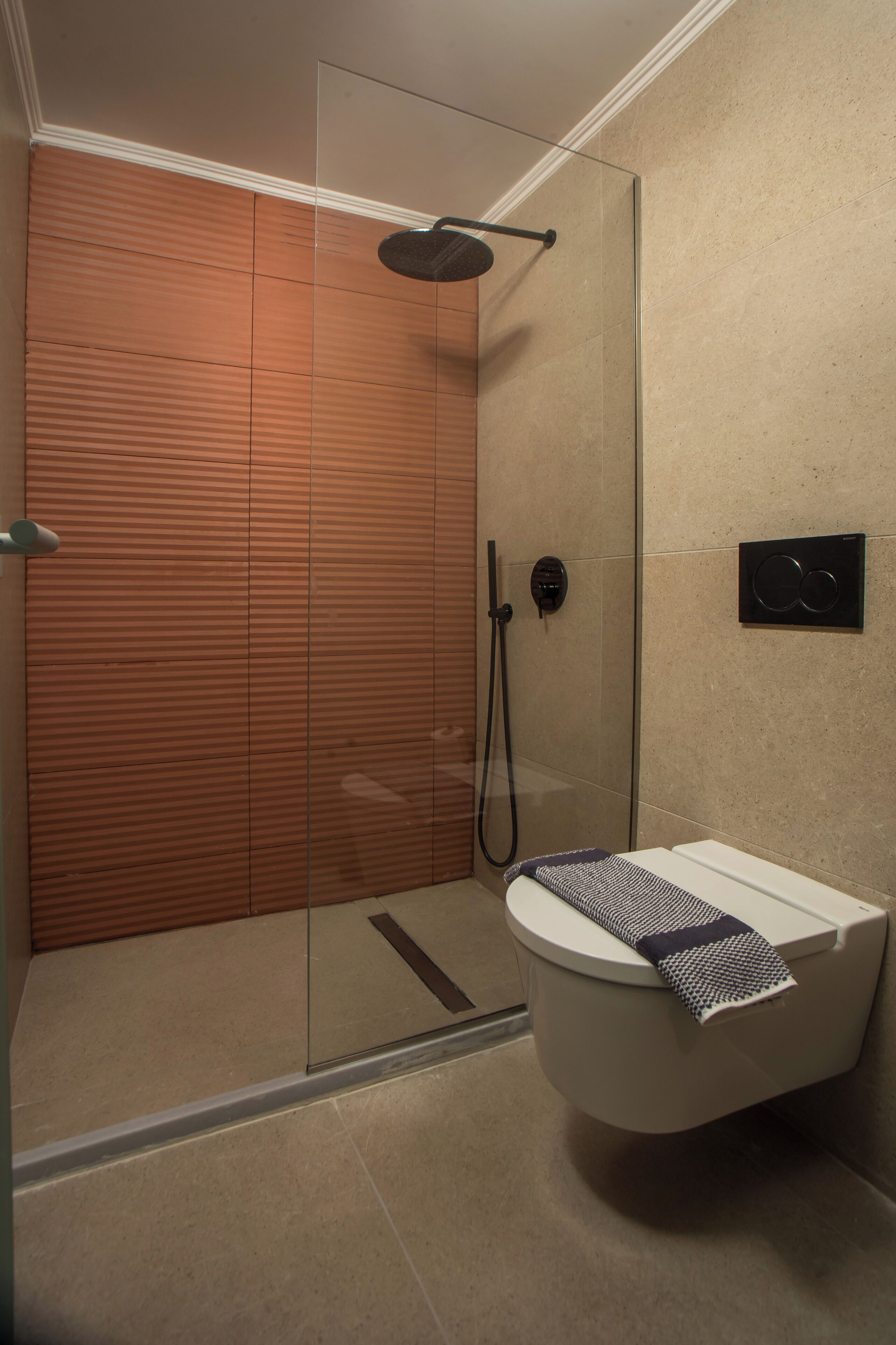 Un baño moderno con cabina de ducha de vidrio, un inodoro con toalla y un panel de control en la pared.