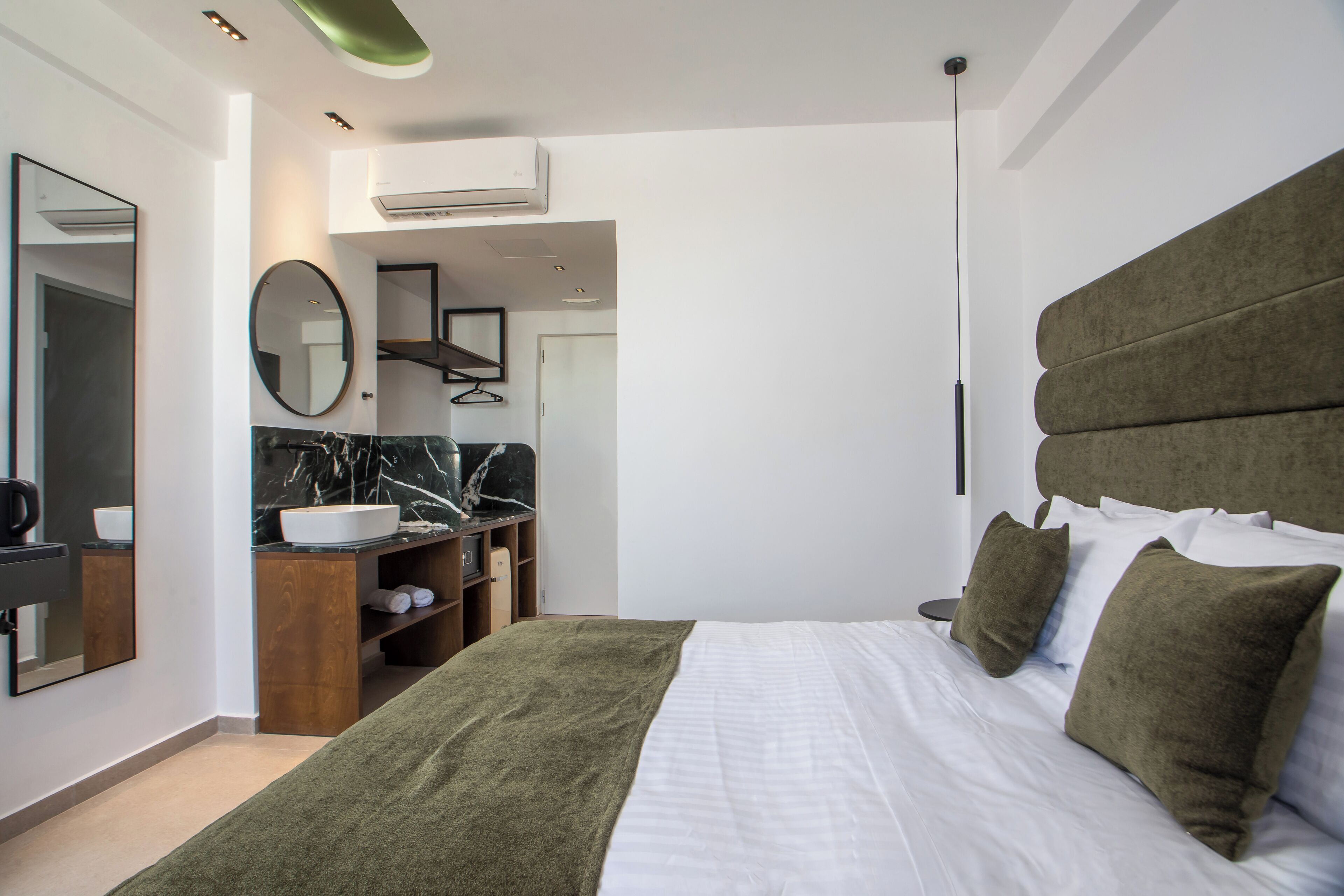 A modern hotel room with a large bed, a vanity with a marble countertop, a mirror, and a green headboard.