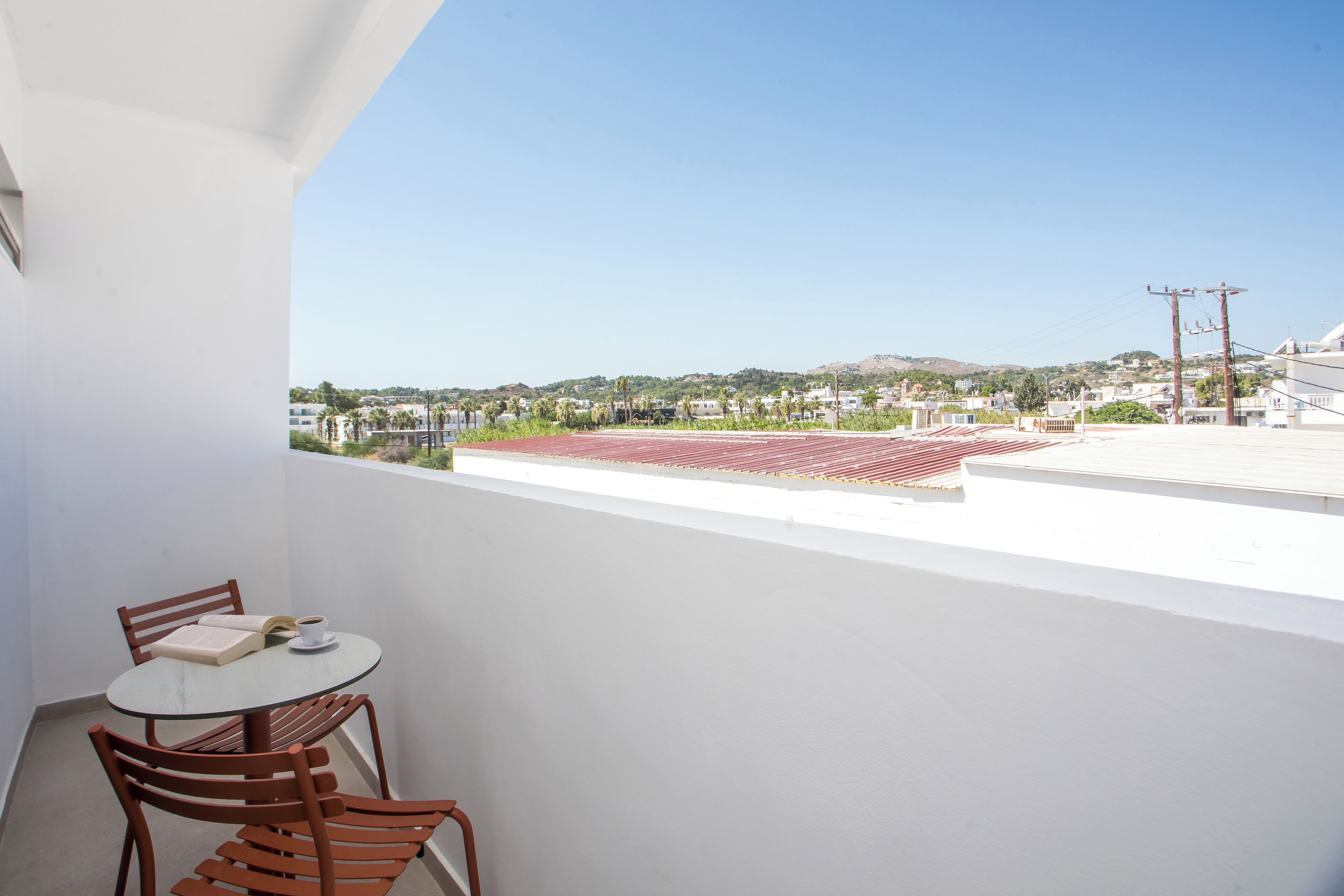 A balcony with a table and chairs, overlooking a cityscape with buildings and a hill.