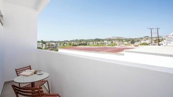 A balcony with a table and chairs, overlooking a cityscape with buildings and a hill.