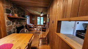 Interior acogedor de una cabaña con una pared de piedra, mobiliario de madera y una cocina visible a través de una ventana.