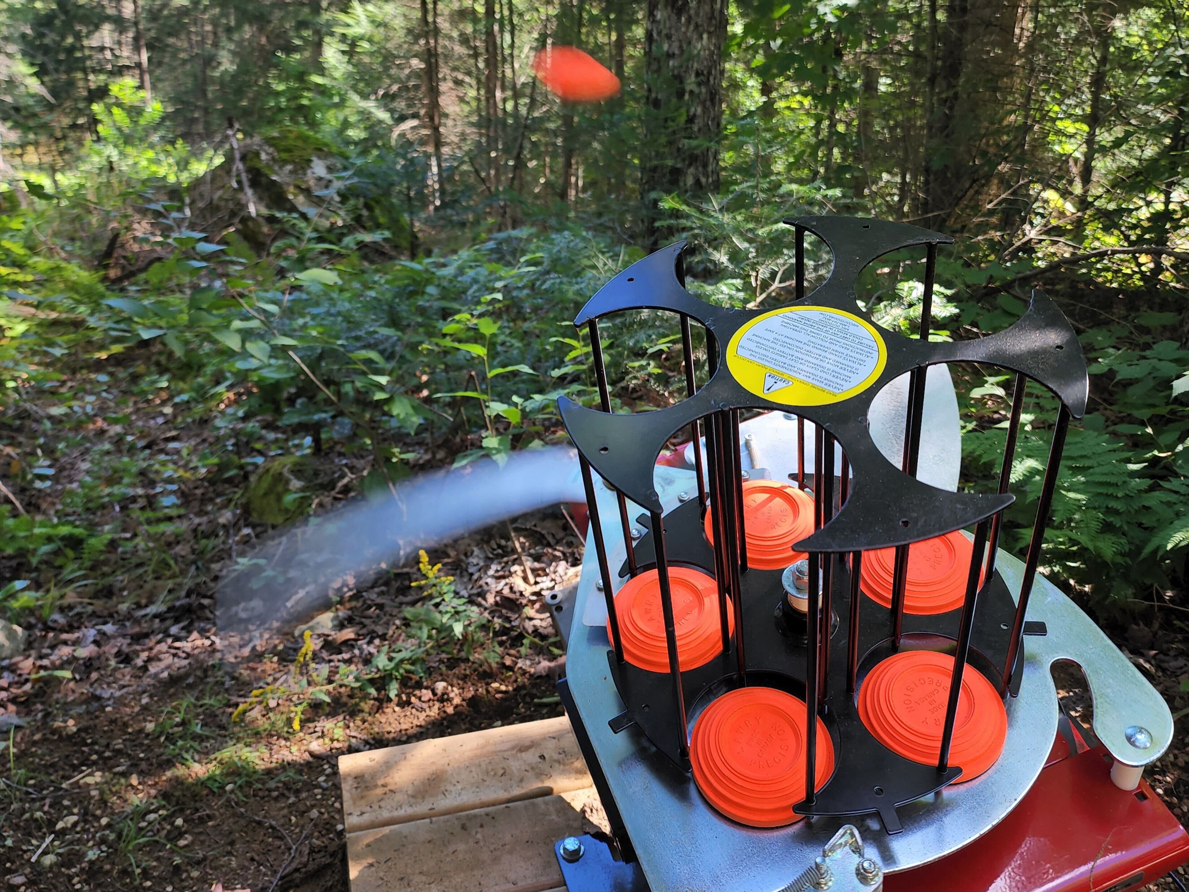 A mechanical device with multiple orange discs, a metal structure, and a pipe emitting steam or smoke.