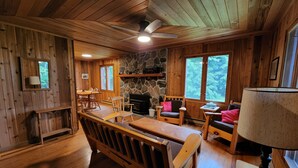L’intérieur chaleureux d’un chalet avec des murs en bois, une cheminée en pierre, un coin repas et un espace détente avec une table et des chaises.