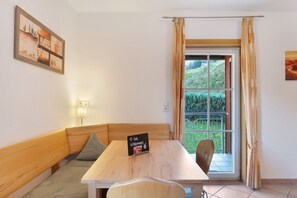A room with a wooden bench, a table, a sign, a window with curtains, and a painting on the wall.