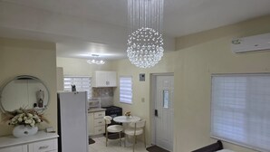 A compact hotel room with a kitchenette, a bed, a round mirror, and a decorative chandelier.
