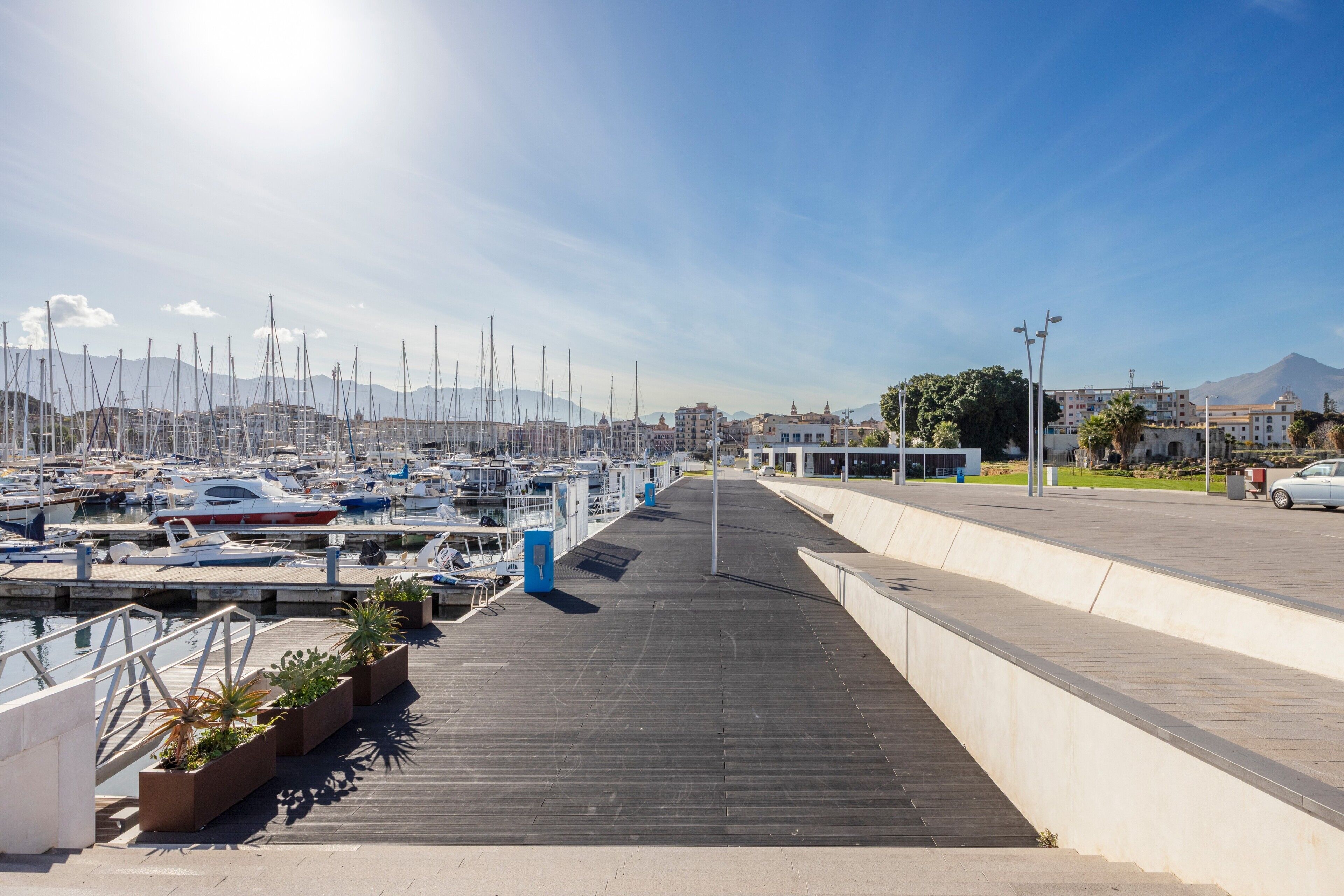 A marina with boats docked, a wooden walkway, and buildings in the background.