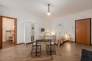 Une pièce comprenant un lit, une table avec des chaises, une porte en bois et une armoire blanche.