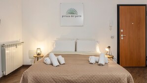 A hotel room with a bed, two bedside tables with lamps, a wooden door, and a sign on the wall. - Apartment 'Del Porto, Palermo' with Balcony, Wi-Fi and Air Conditioning (Palermo)