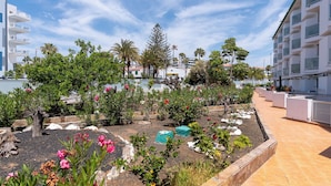 Un área ajardinada con diversas plantas y flores, una estructura de madera y un sendero con baldosas.