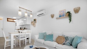 Una sala de estar moderna con un sofá blanco, cojines color turquesa, una mesita de centro pequeña y un comedor con una mesa y sillas blancas.