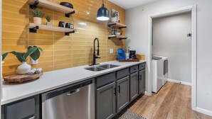 A modern kitchen with stainless steel appliances, wooden shelves, and a patterned rug.