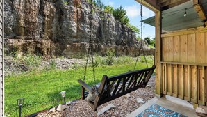 A wooden bench with a view of a rocky cliff, a wooden fence, and a patterned rug on the ground.