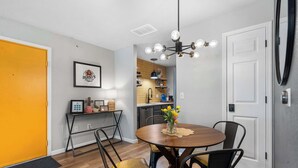 A dining area with a round table, chairs, a chandelier, and a kitchen in the background.
