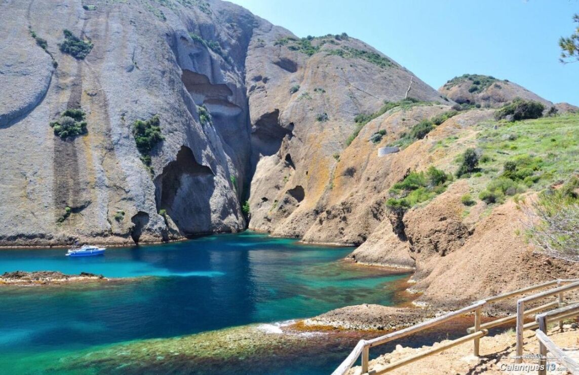 A coastal landscape with a large rock formation, a clear blue sea, and a small boat.