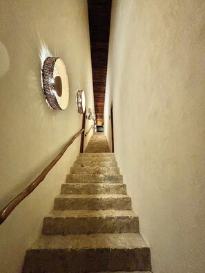 Un escalier en pierre avec une rampe en bois et un mur à texture sur le côté gauche.
