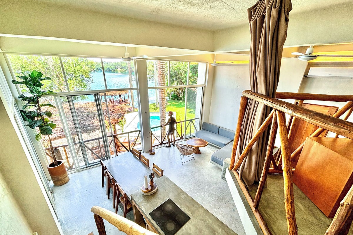 A spacious balcony with a view of a pool and greenery, a dining area with a table and chairs, and a staircase with wooden railings.