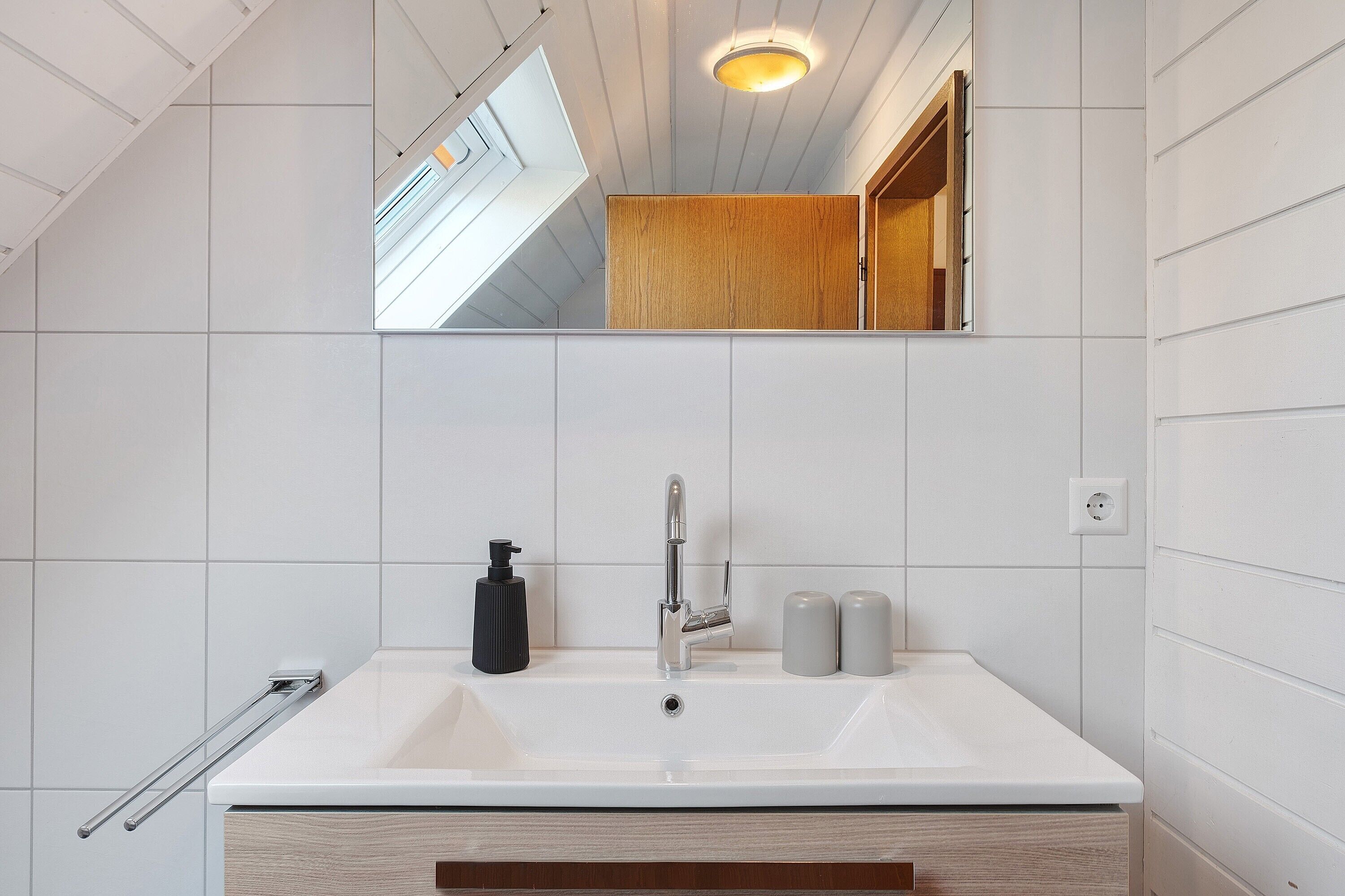 Een badkamer met een witte wastafel, een spiegel, een houten kastje en een dakraam.