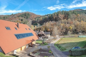 Ein Gebäude mit rotem Dach, einem Garten und Blick auf einen bewaldeten Hügel.