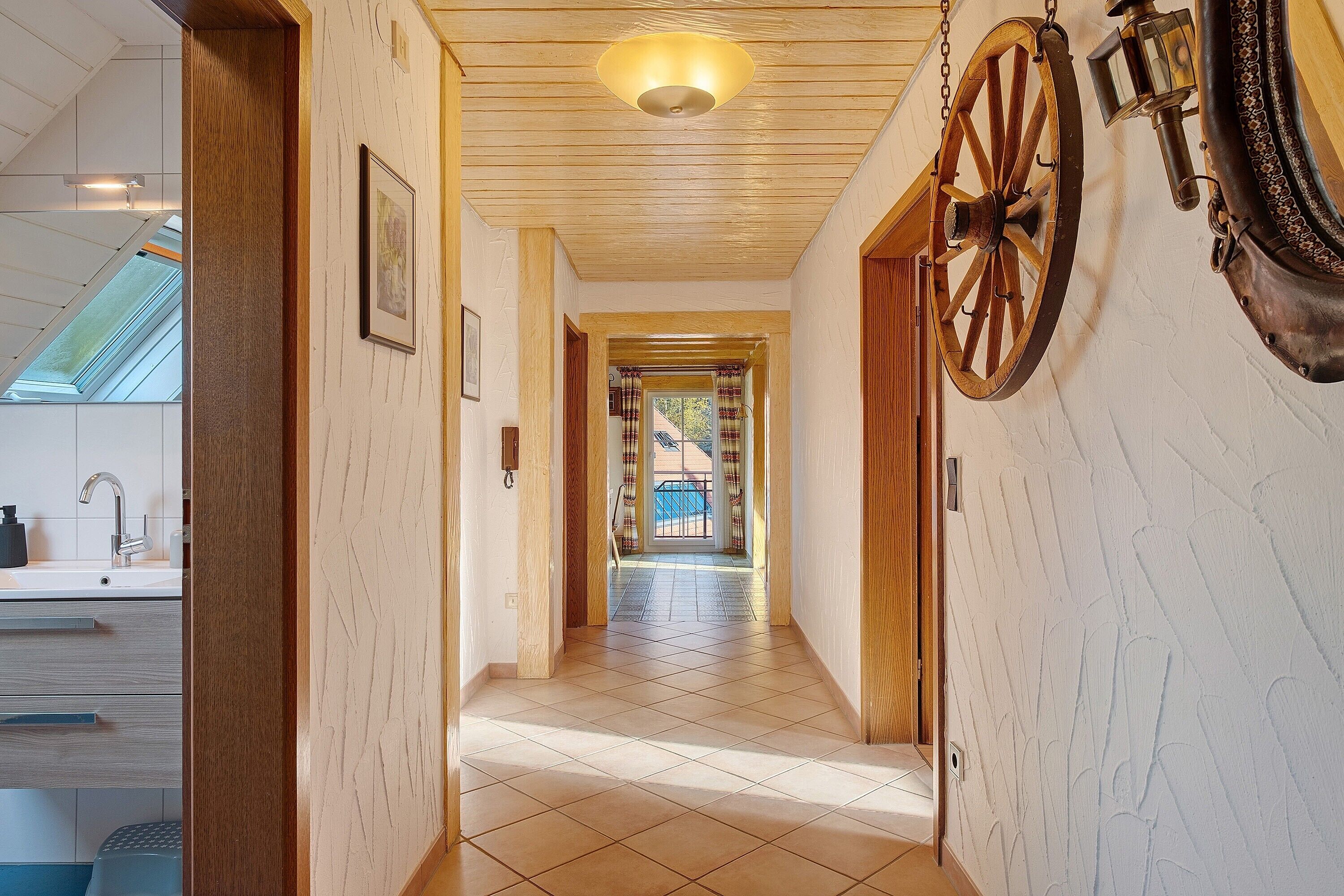 Un couloir avec un plafond en bois, une grande roue en bois et une vue sur un balcon.