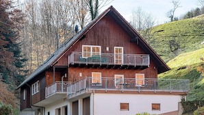 A two-story wooden building with a balcony, a covered entrance, and a hillside backdrop. - Holiday Apartment 'Kirschblüte' with Mountain View, Shared Pool and Wi-Fi (Wolfach)