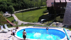 A swimming pool with a clear blue water, surrounded by a stone deck, and a grassy area with a pathway leading to a building. - Holiday Apartment 'Kirschblüte' with Mountain View, Shared Pool and Wi-Fi (Wolfach)