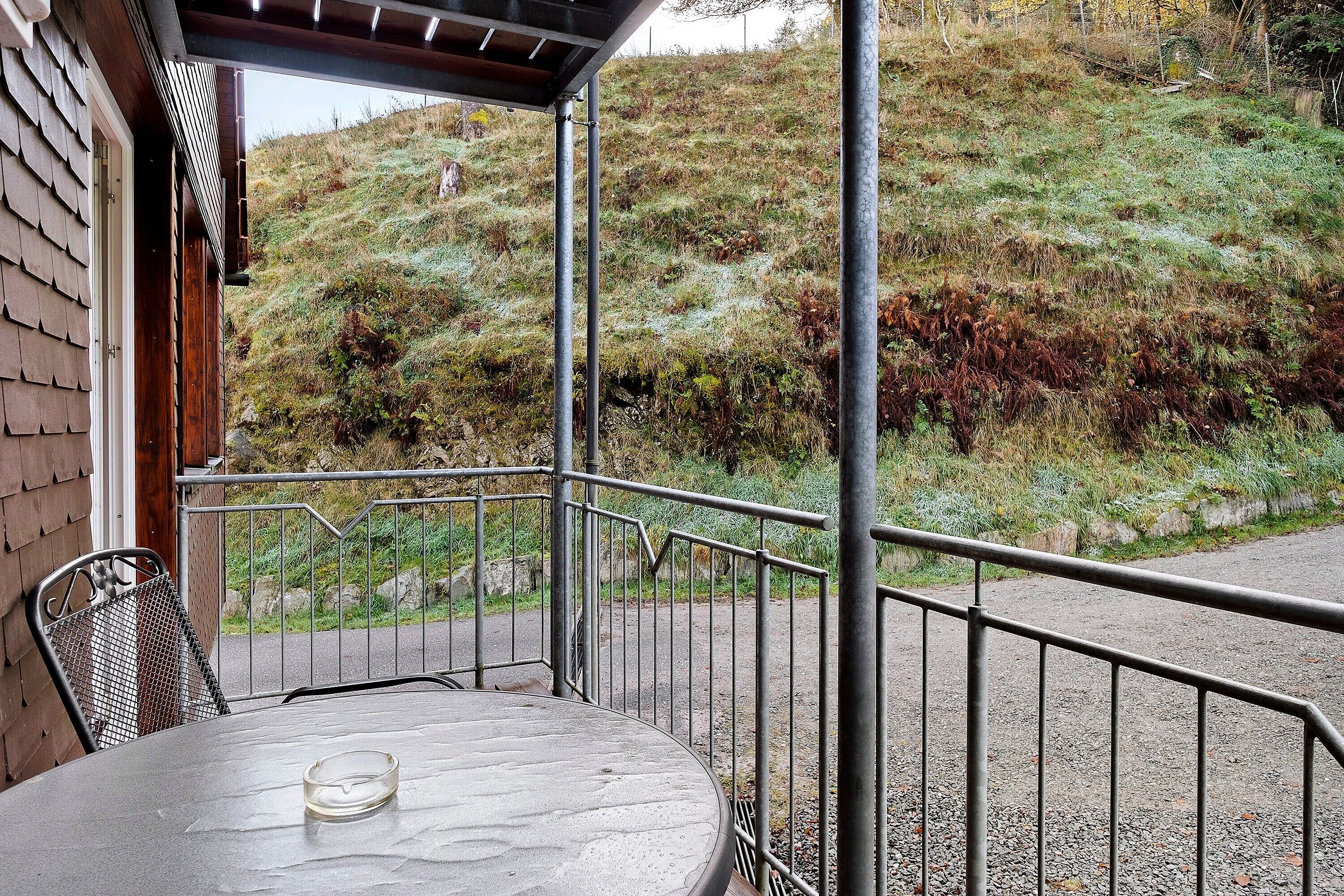 A patio with a table and chairs, a metal railing, and a view of a hillside.