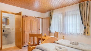 A room with two beds, a wooden ceiling, a wooden wardrobe, a wooden table, a mirror, and a window with curtains. - Holiday Apartment 'Kirschblüte' with Mountain View, Shared Pool and Wi-Fi (Wolfach)