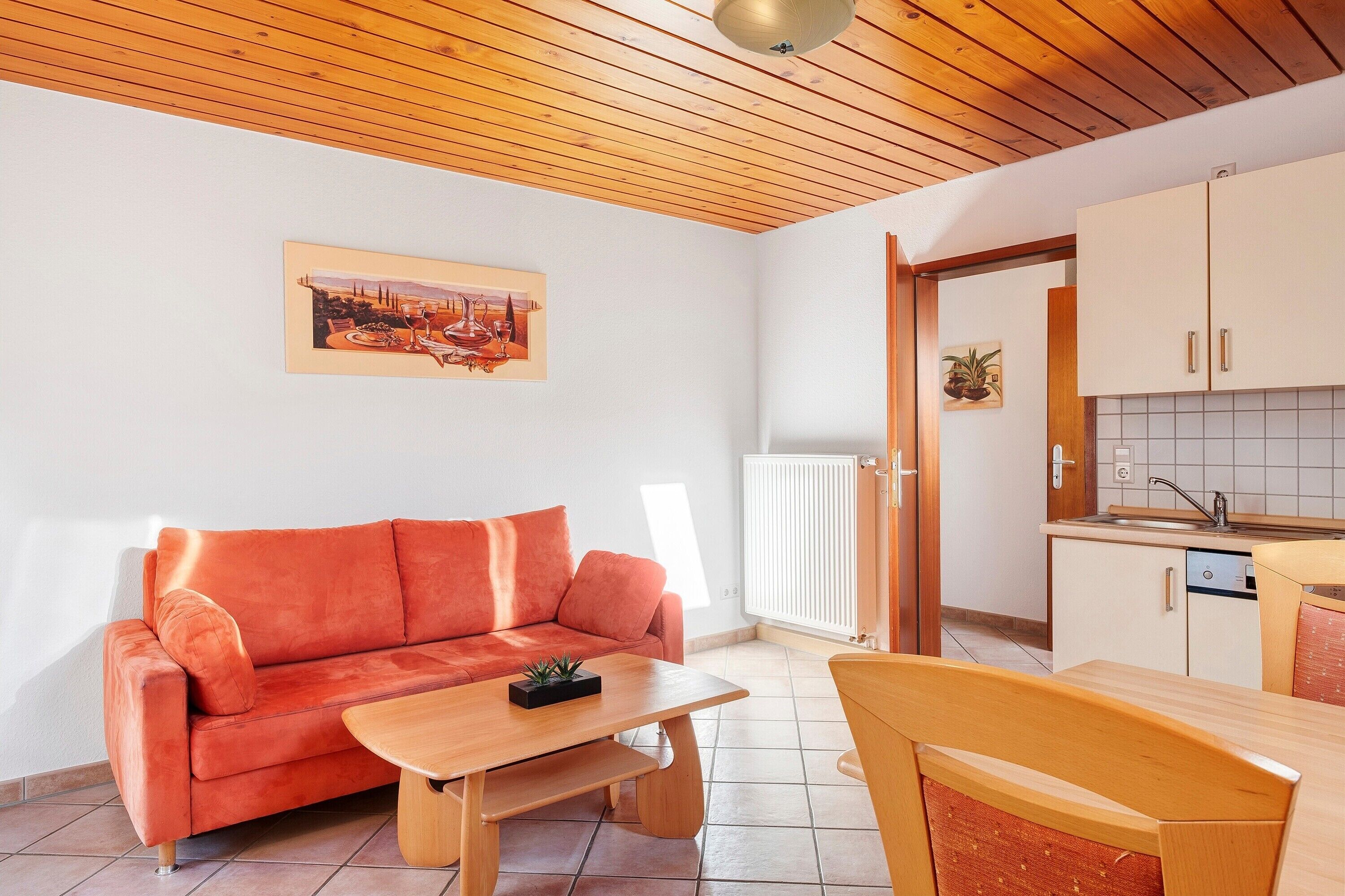 Een woonkamer met een bank, een houten tafel en een keukenhoek met kastjes en een radiator.