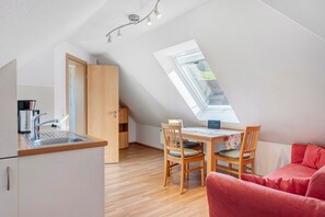 A compact room with a kitchenette, a dining area with a table and chairs, a red sofa, and a skylight.