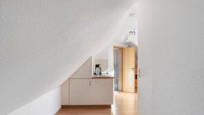 A narrow hallway with a kitchen area at the end, featuring white walls, wooden flooring, and a visible door leading to another room. - Apartment 'Vogelnest' with Mountain View, Shared Pool and Wi-Fi – Not Suitable for Dogs (Wolfach)
