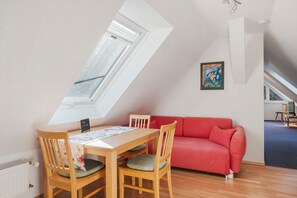 A room with a sloped ceiling, a dining table with chairs, a red sofa, and a painting on the wall.