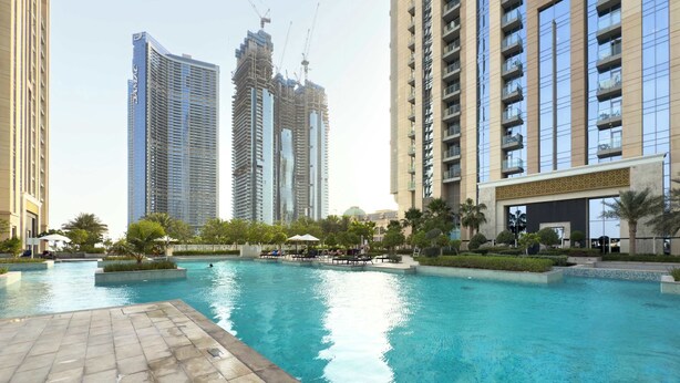 A swimming pool area with a tiled deck, surrounded by high-rise buildings and palm trees. - 2BR Waterfront Apartment  Nr Downtown (Business Bay)