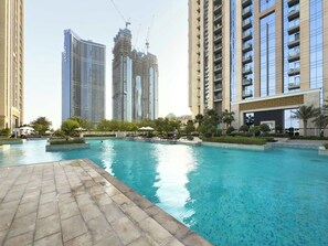 Un área de piscina con suelo de baldosas, rodeada de edificios altos y palmeras.