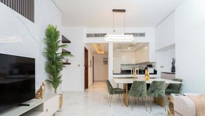 A modern living room with a flat-screen TV, a dining area with a table and chairs, and a kitchen in the background. - 2BR Waterfront Apartment  Nr Downtown (Business Bay)