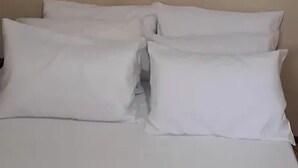 Un lit avec une literie et des oreillers blancs, un mur sobre et un tableau au-dessus du lit.