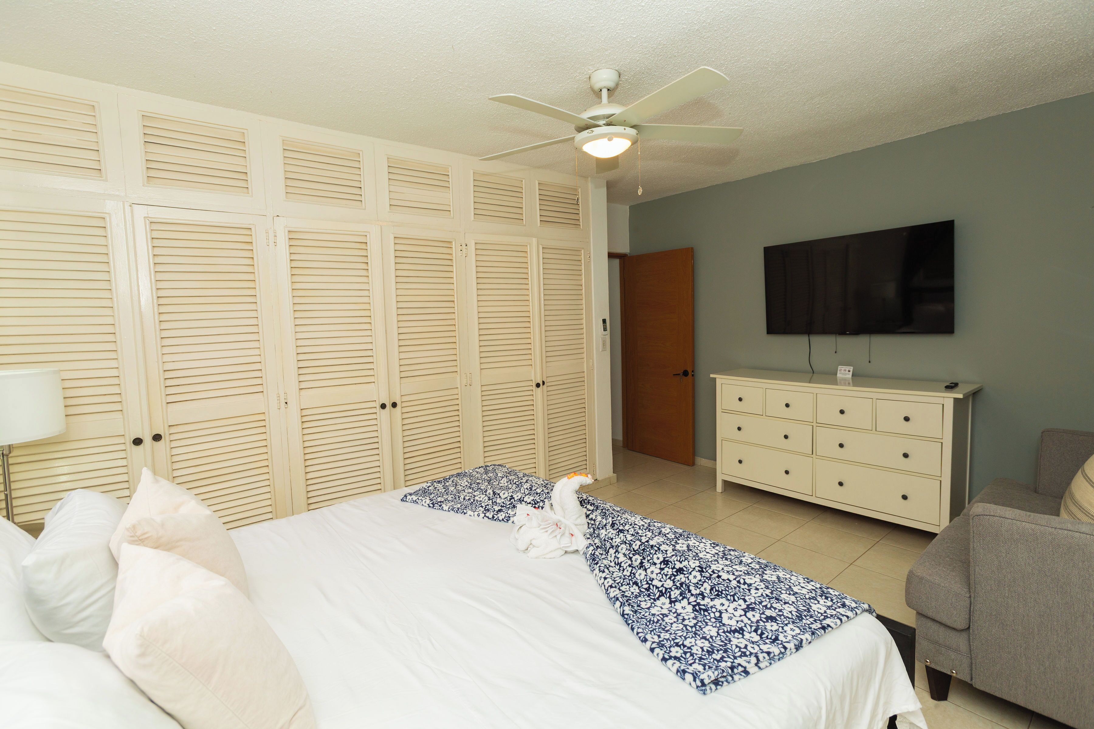 Ein Schlafzimmer mit Bett, Kommode, Fernseher und Deckenventilator.