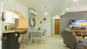 Ein modernes Wohnzimmer mit Küchenzeile, einem Esstisch mit Stühlen, einer Couch und einem Fernseher.
