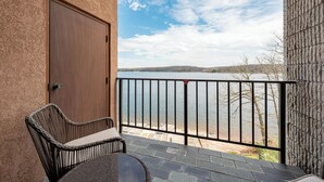 Een balkon met uitzicht op een meer, een rieten stoel en een deur.