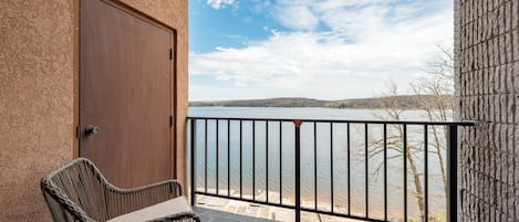 A balcony with a view of a lake, a wicker chair, and a door.