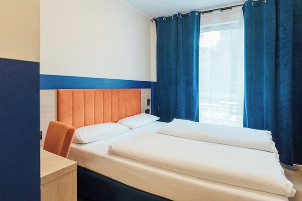 A hotel room with a bed, a desk, and a window with curtains. - MYKY Hotel Boardinghouse  (Hamburg)
