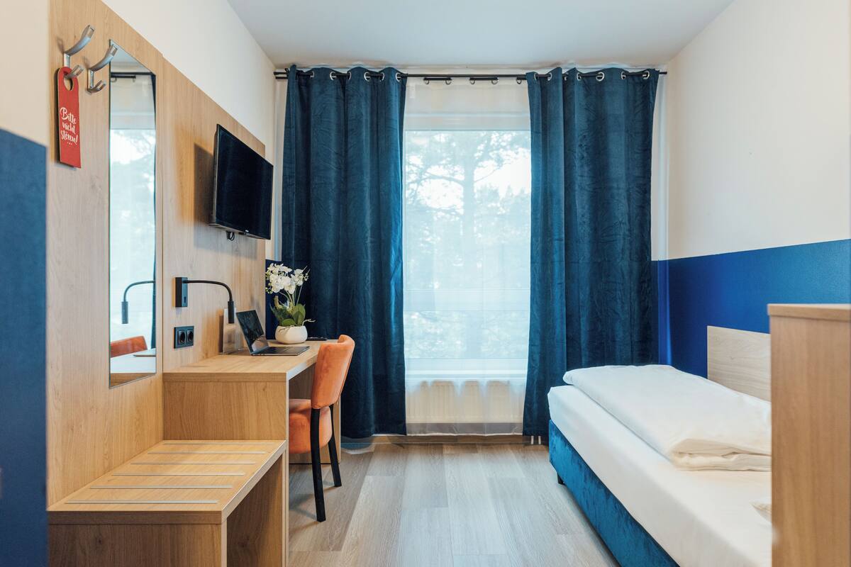 A hotel room with a wooden desk, a chair, a bed, and a TV mounted on the wall.