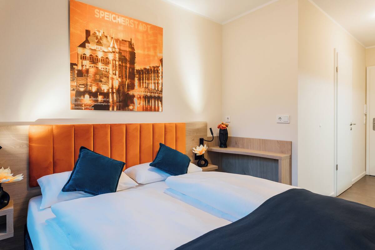 A hotel room with a large bed, a nightstand with a vase of flowers, and a poster of a building on the wall.