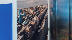 Interior de un hotel con un cartel de paisaje urbano, un ascensor y una alfombra estampada.