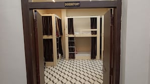 A dormitory with bunk beds, a tiled floor, and a 'DORMITORY' sign above the entrance. - Kashi Vandanam (Varanasi)