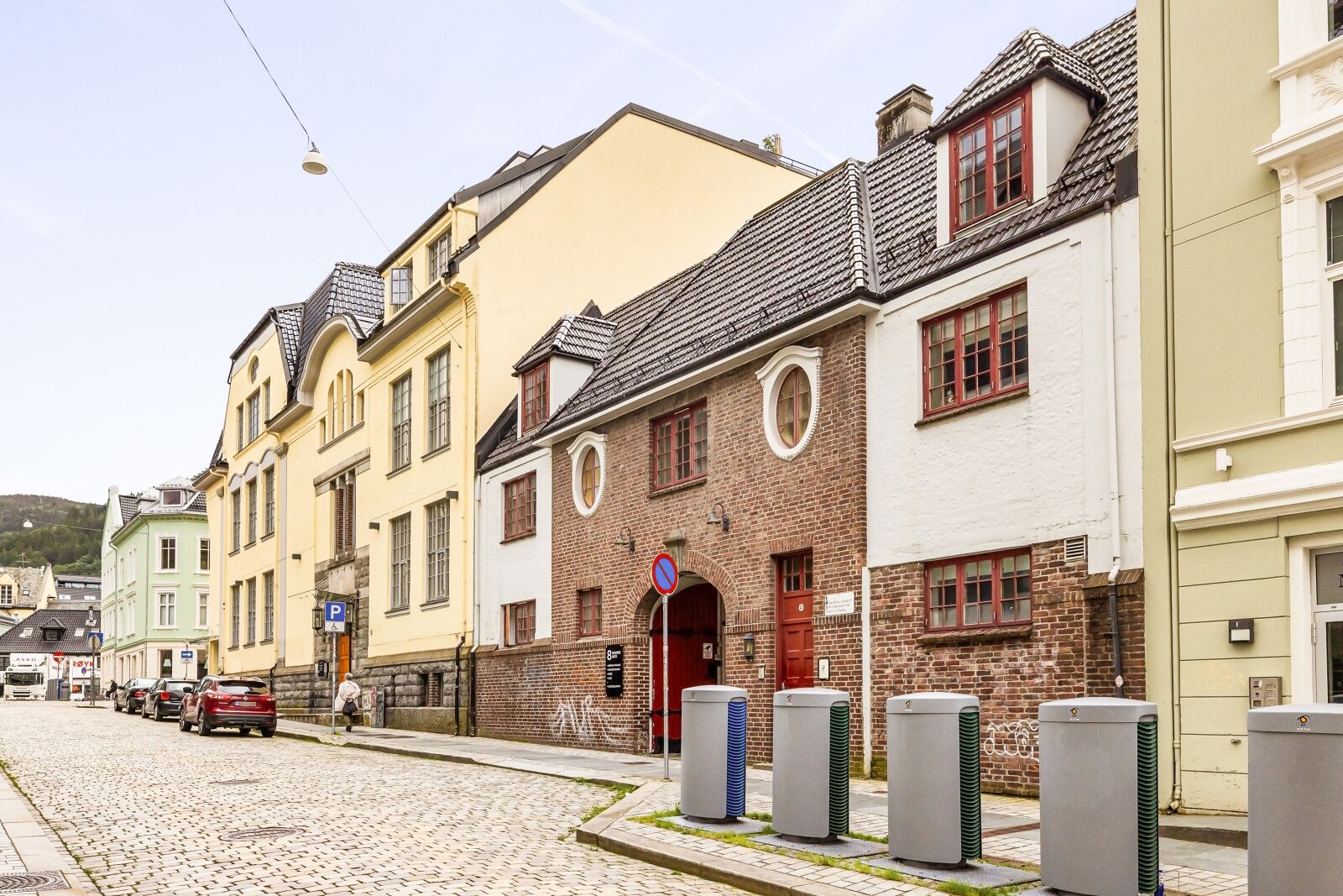 Une rue pavée bordée de bâtiments historiques, un panneau de signalisation indiquant un espace de stationnement et des unités de climatisation extérieures.
