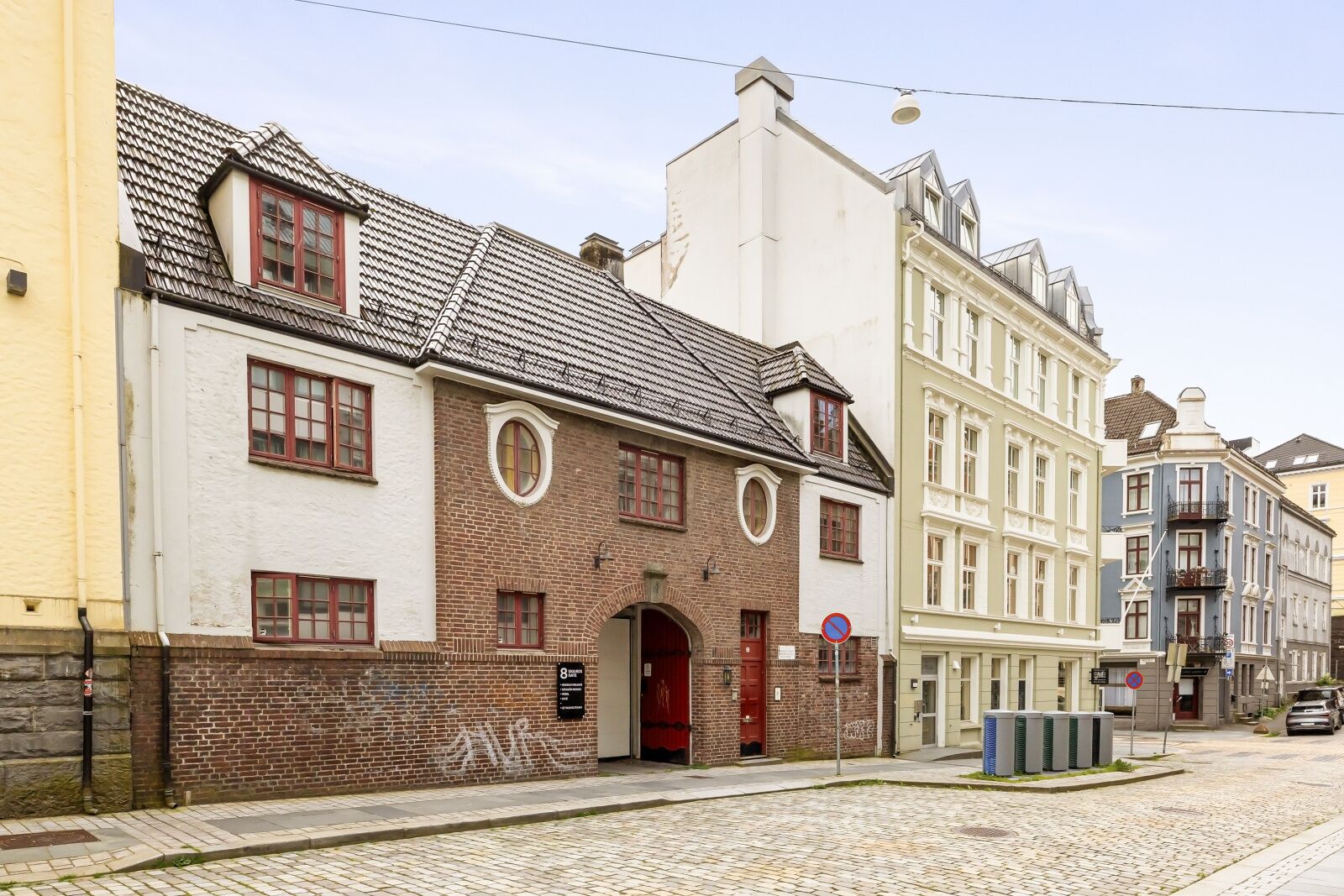 Une rue historique bordée de bâtiments à l’architecture traditionnelle, avec une chaussée pavée et un panneau indiquant qu’il est interdit de se garer.