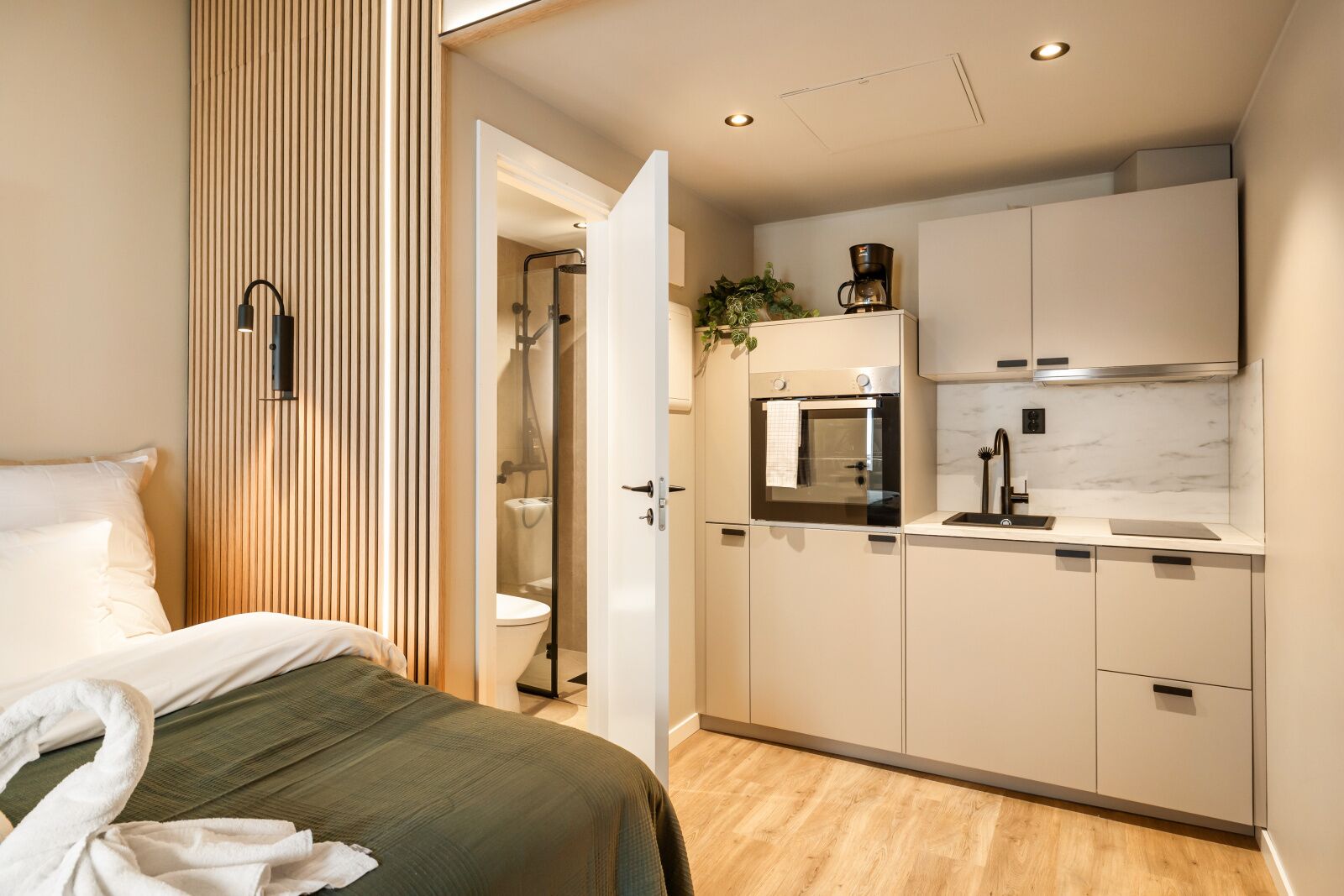 A modern hotel room with a bed, a shower, a kitchenette, and a bathroom.