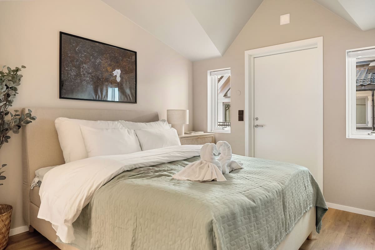 Una cama bien hecha con colcha verde, un cuadro en la pared y una puerta que da a otra habitación.