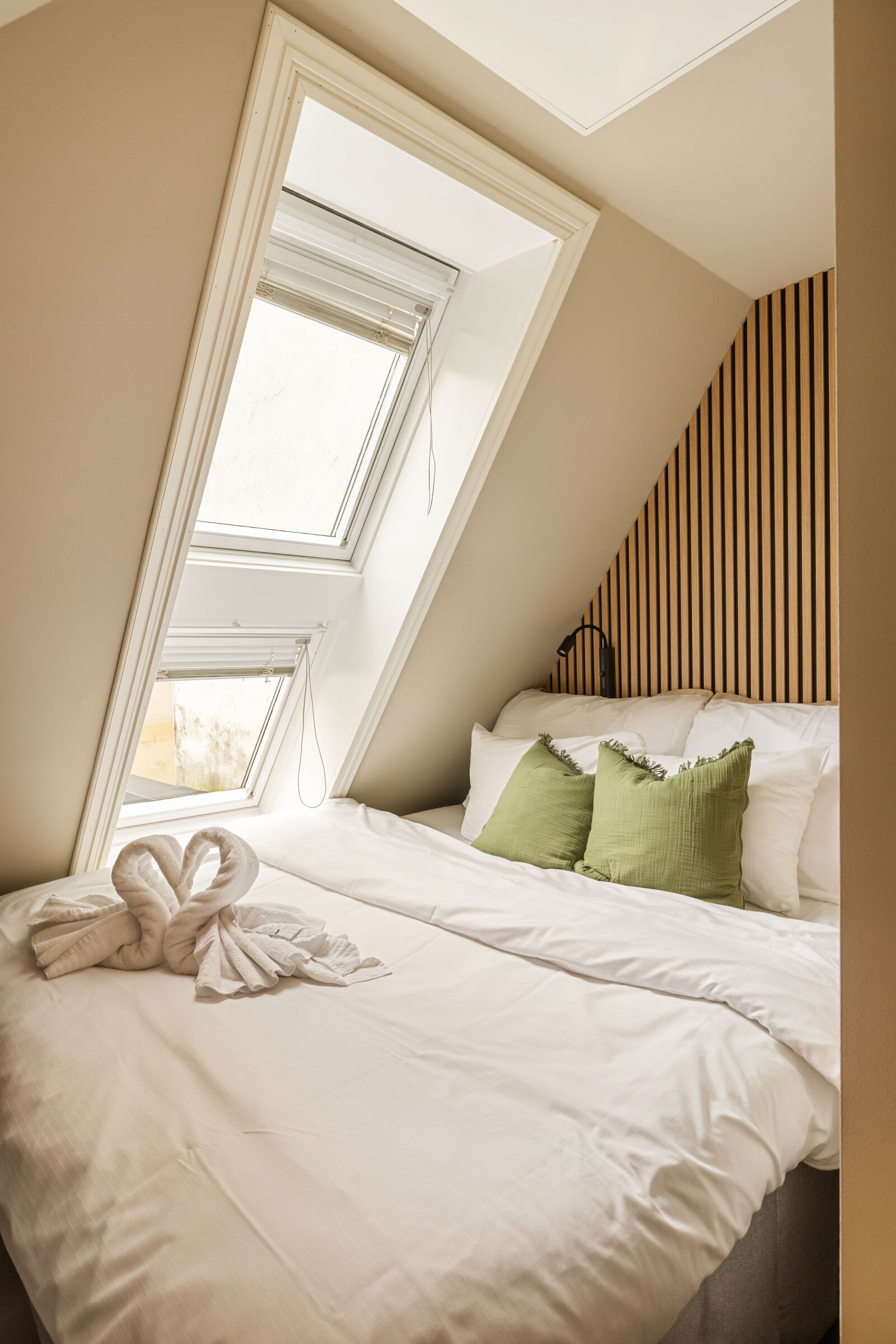 A bedroom with a skylight, a bed with white and green pillows, and a towel on the bed.